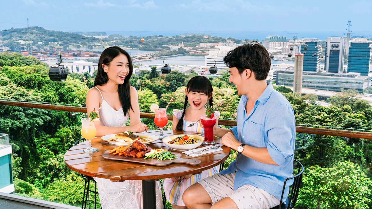 Tourists dining in a cable car, enjoying views of Singapore's skyline.