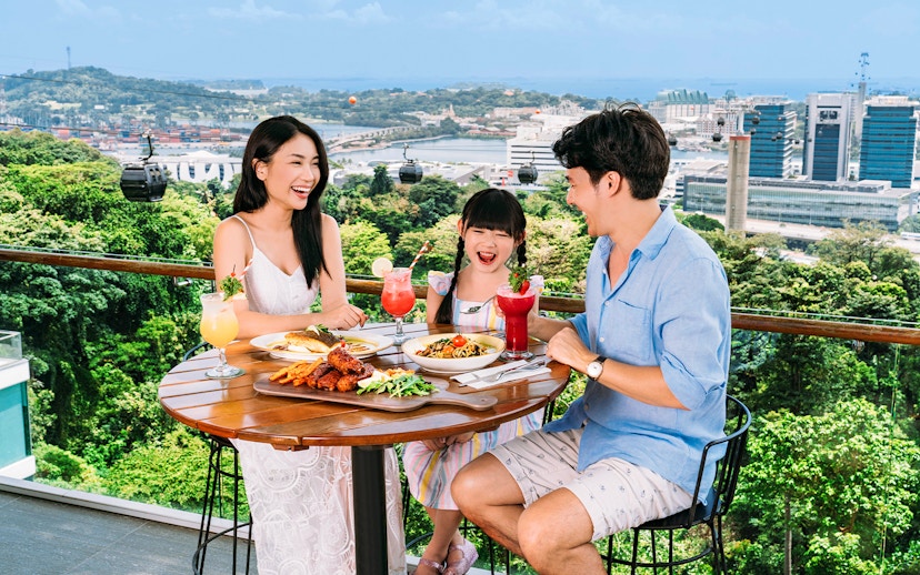 Tourists dining on Singapore Cable Car Sky Pass with city skyline view.