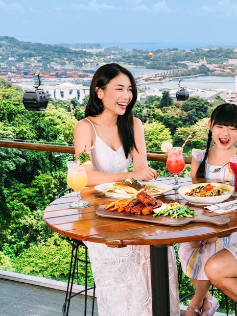 Tourists dining on Singapore Cable Car Sky Pass with city skyline view.