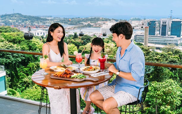 Tourists dining on Singapore Cable Car Sky Pass with city skyline view.