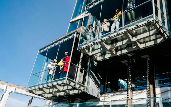 Visitors in glass elevators at SUMMIT Ascent Experience, enjoying city views.