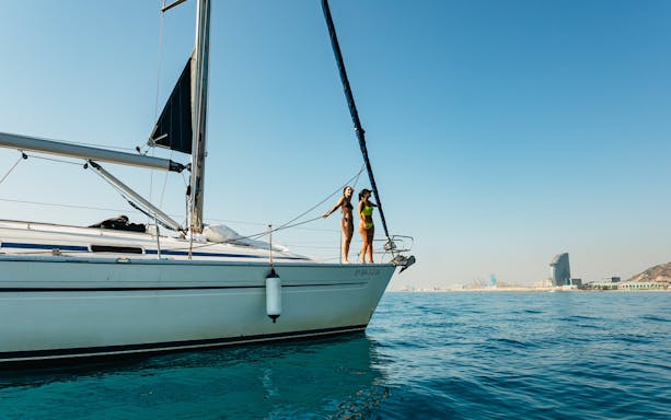 Friends on a sailing yacht enjoying a Barcelona sightseeing cruise with city skyline in view.