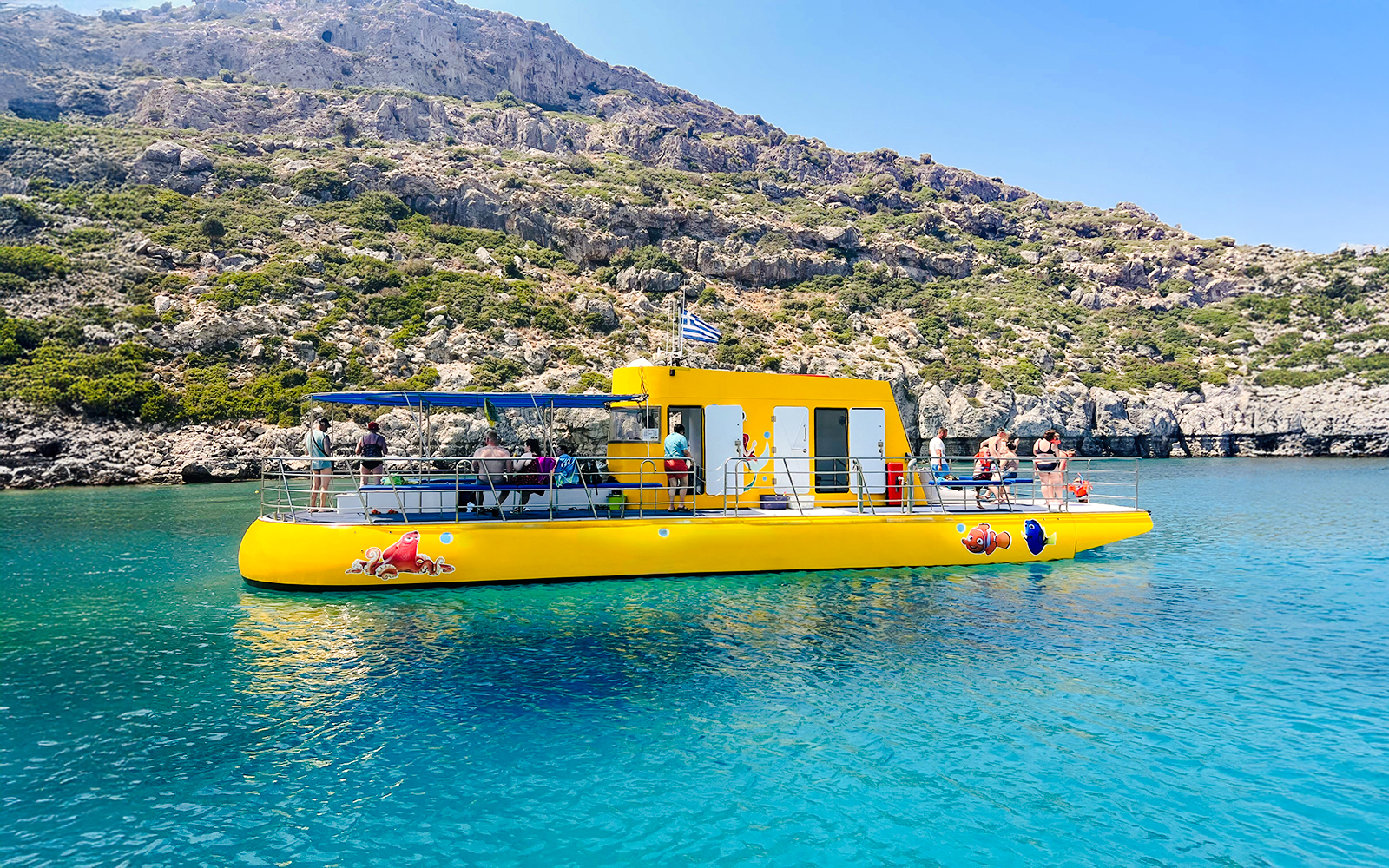 Yellow submarine cruise with tourists near rocky coast in Rhodes.