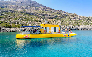 Yellow submarine cruise with tourists near rocky coast in Rhodes.