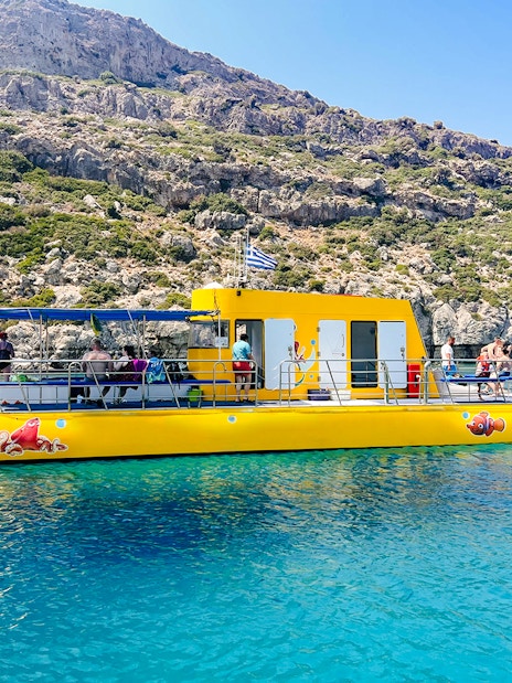 Yellow submarine cruise with tourists near rocky coast in Rhodes.