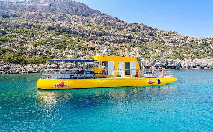 Yellow submarine cruise with tourists near rocky coast in Rhodes.