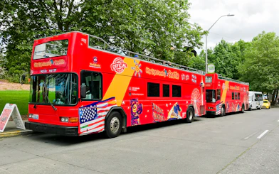 Red double-decker tour bus in Seattle with sightseeing graphics parked by trees.