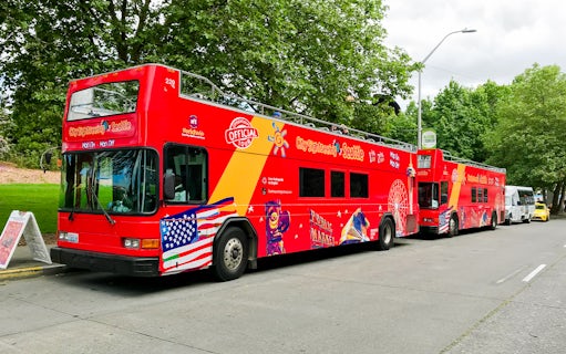 Red double-decker tour bus in Seattle with sightseeing graphics parked by trees.