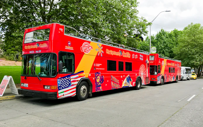 Red double-decker tour bus in Seattle with sightseeing graphics parked by trees.