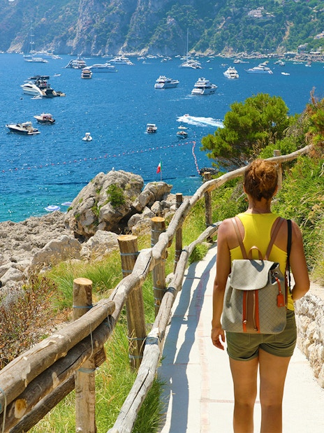 Tourist walking along Capri coastal path with view of boats, part of Rome to Pompeii and Sorrento day trip.