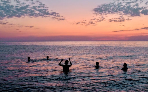 People swimming in the sea during sunset with a colorful sky.