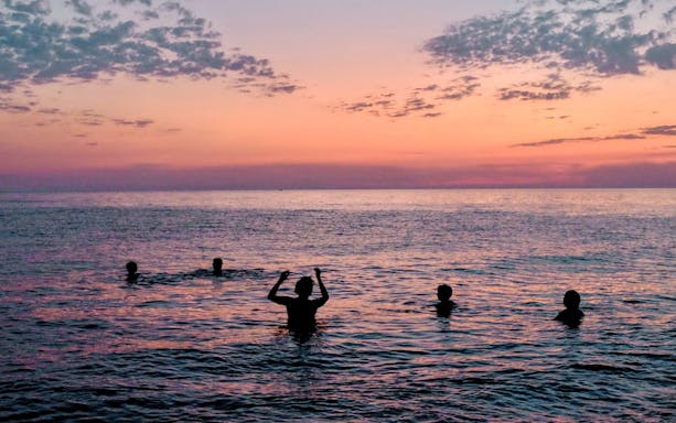 People swimming in the sea during sunset with a colorful sky.