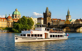Prague river cruise boat passing Charles Bridge with historic buildings in the background.