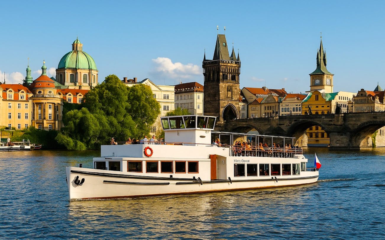Prague river cruise boat passing Charles Bridge with historic buildings in the background.