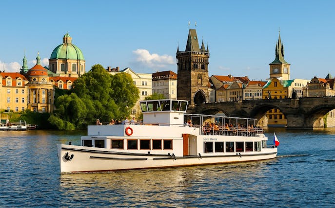 Prague river cruise boat passing Charles Bridge with historic buildings in the background.