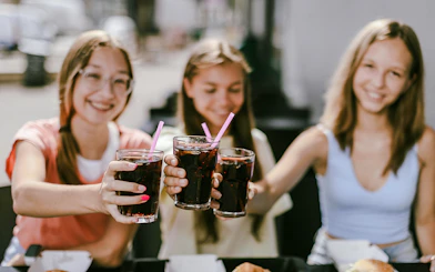 Group of friends toasting with soft drinks at an outdoor cafe.