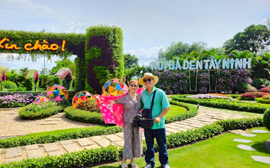 Couple posing at Núi Bà Đen, Tay Ninh, with colorful garden and welcome sign.