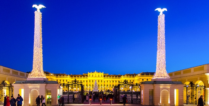 Schonbrunn Palace entrance with Christmas lights and market visitors in Vienna.