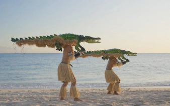 Performers with crocodile costumes on a beach, part of Croc! Lost Giants to Living Legends at Queensland Museum.