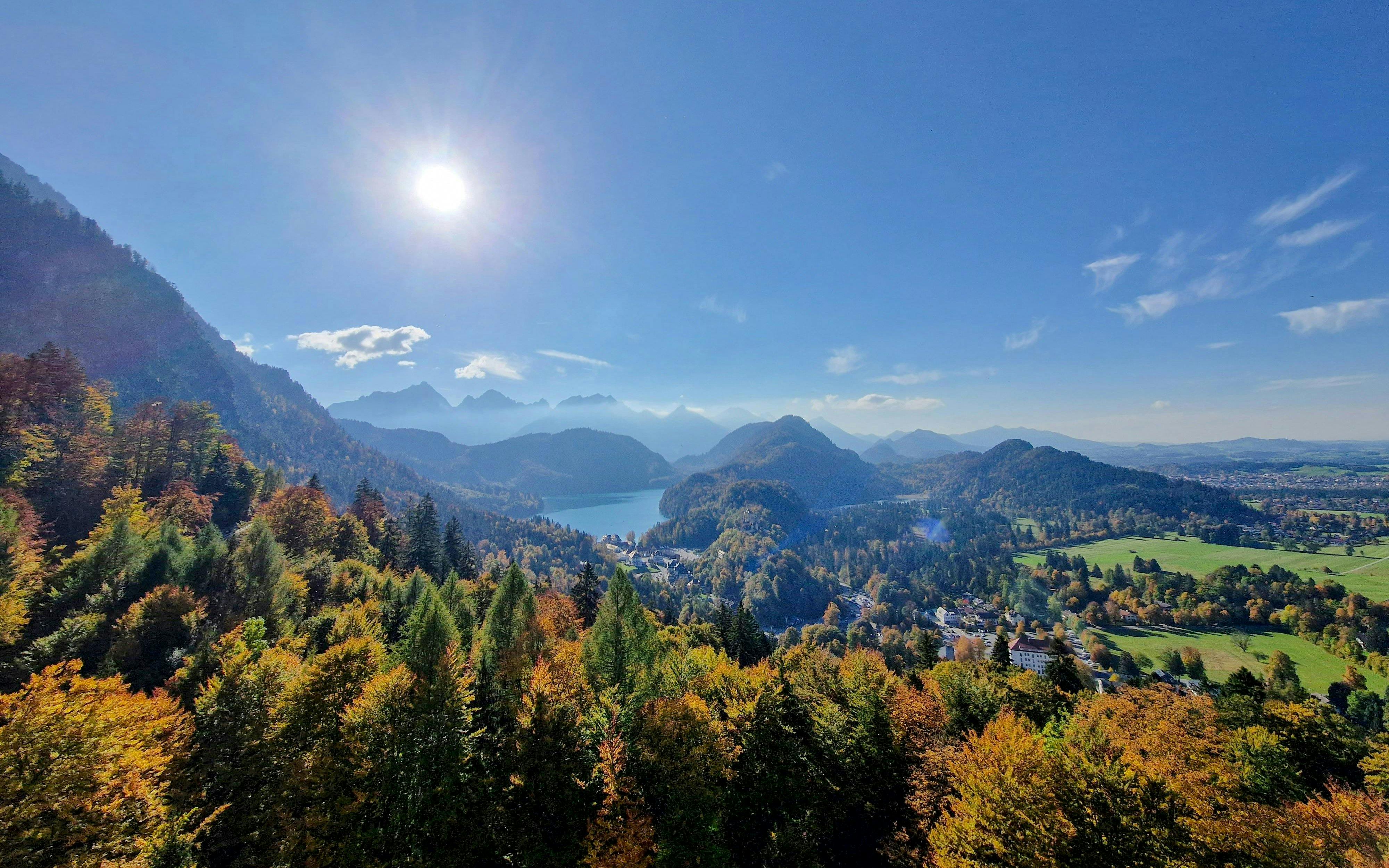 View of Bavarian landscape from Neuschwanstein and Hohenschwangau Castle, featuring forests and mountains.