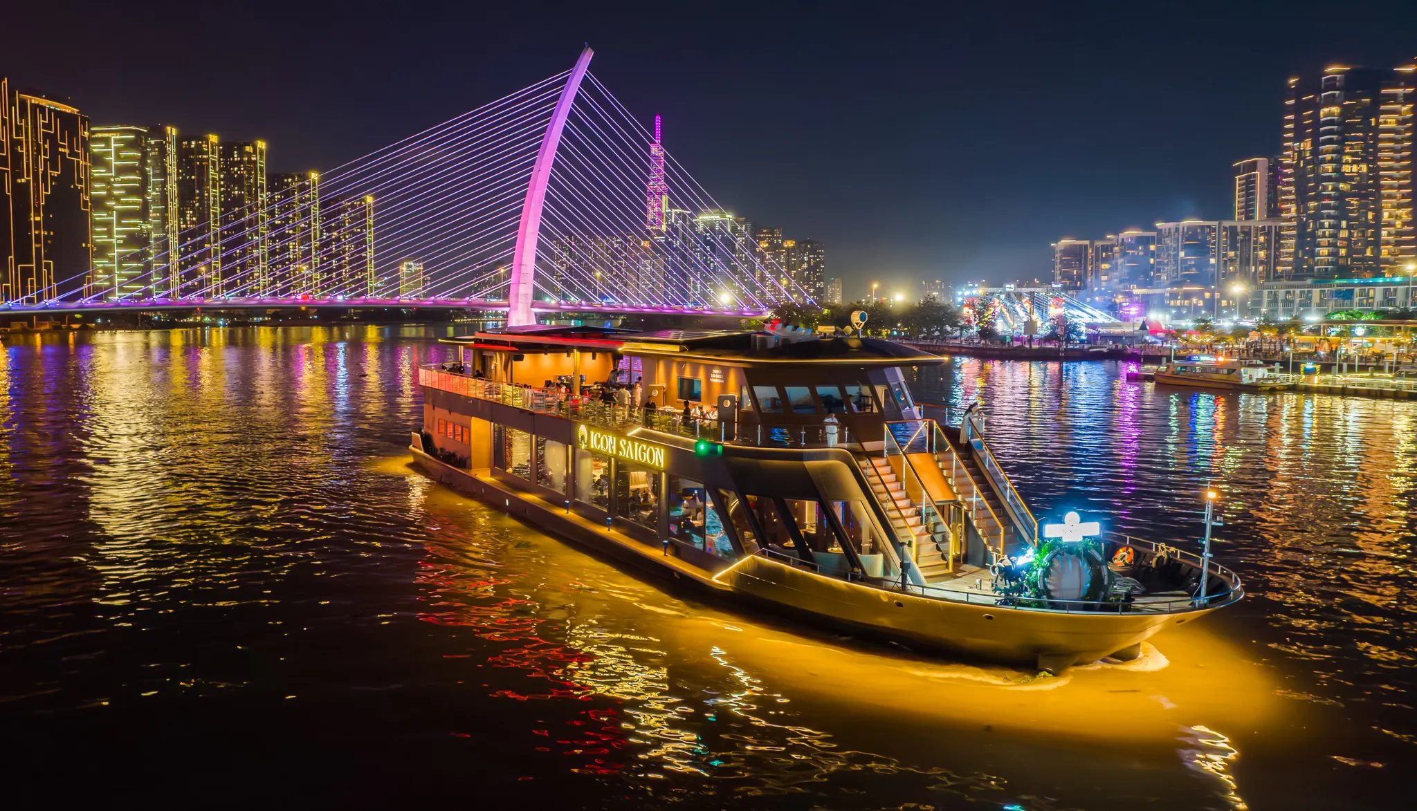 Cruise boat on Saigon River at night with illuminated bridge in Ho Chi Minh City.