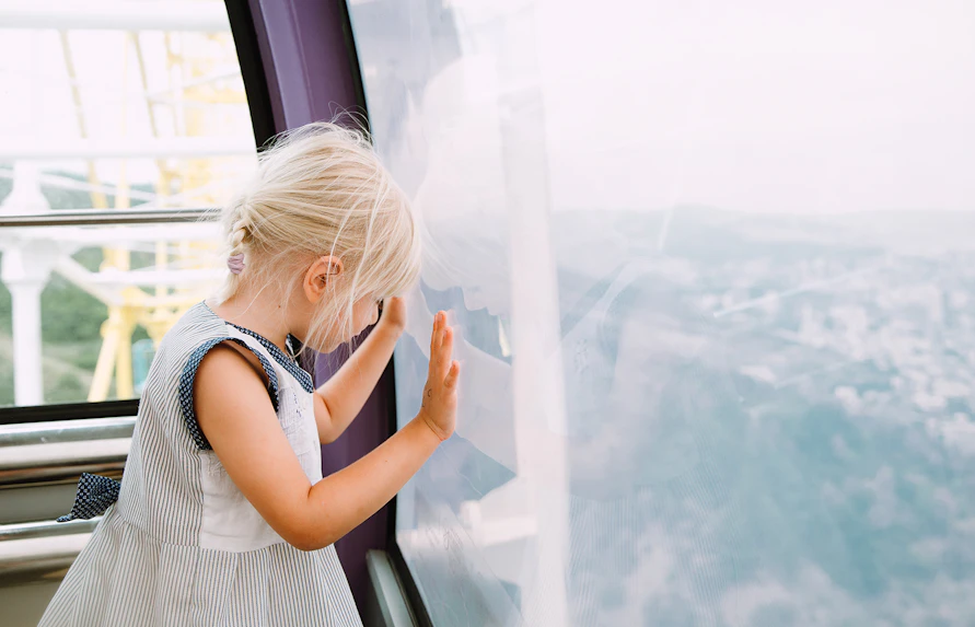Little girl looking out from inside a Ferris wheel cabin.