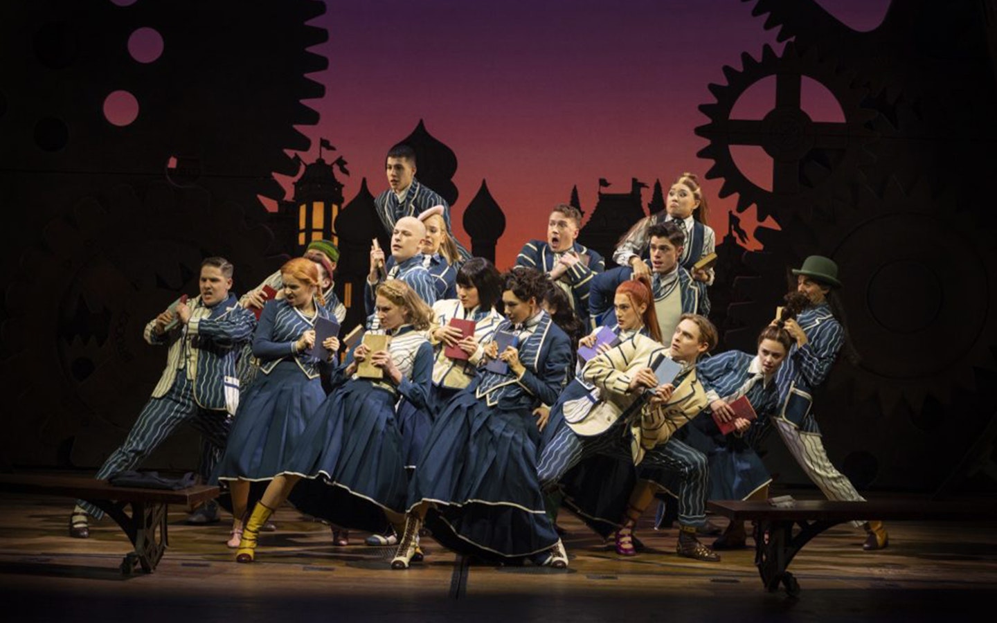 Cast performing a scene from Wicked the Musical with books on stage.