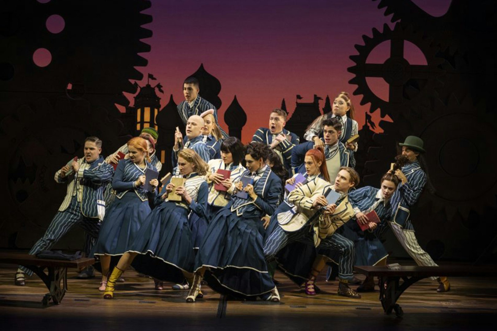 Cast performing a scene from Wicked the Musical with books on stage.