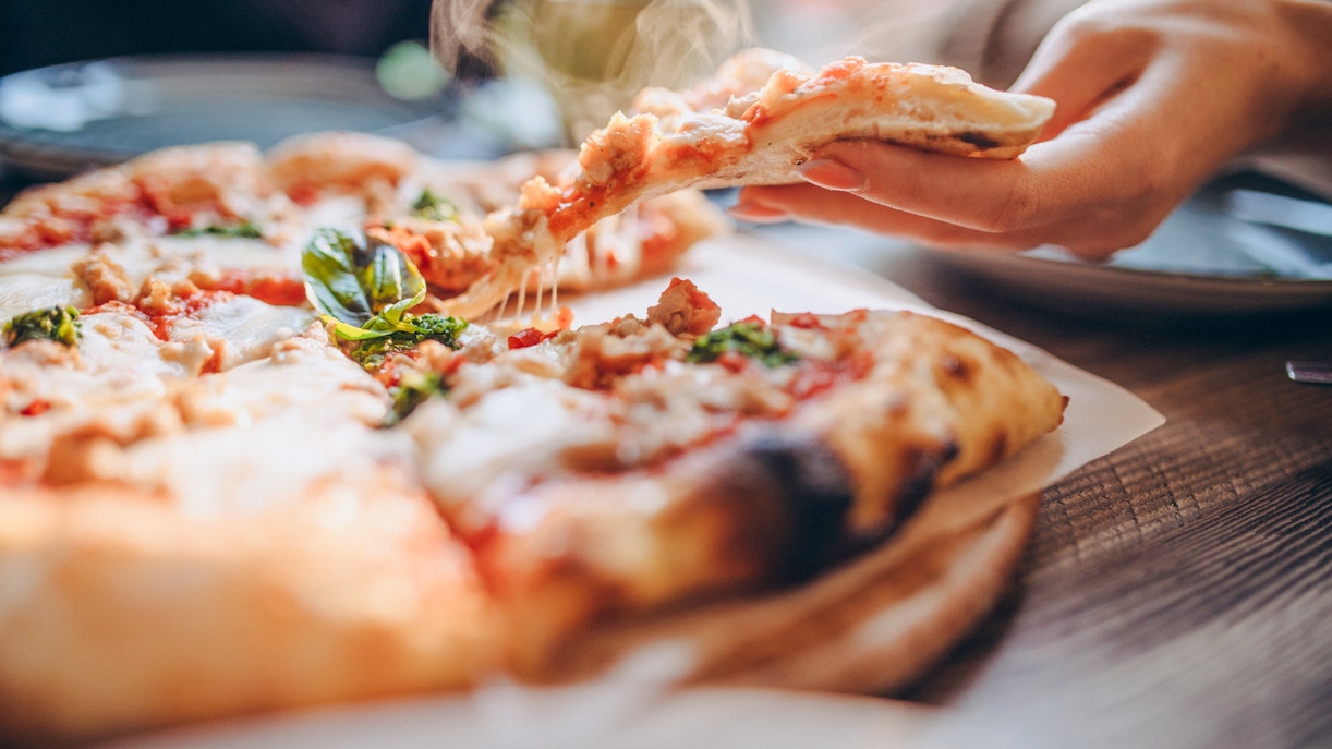Hand holding a slice of Icelandic lamb pizza with fresh basil.