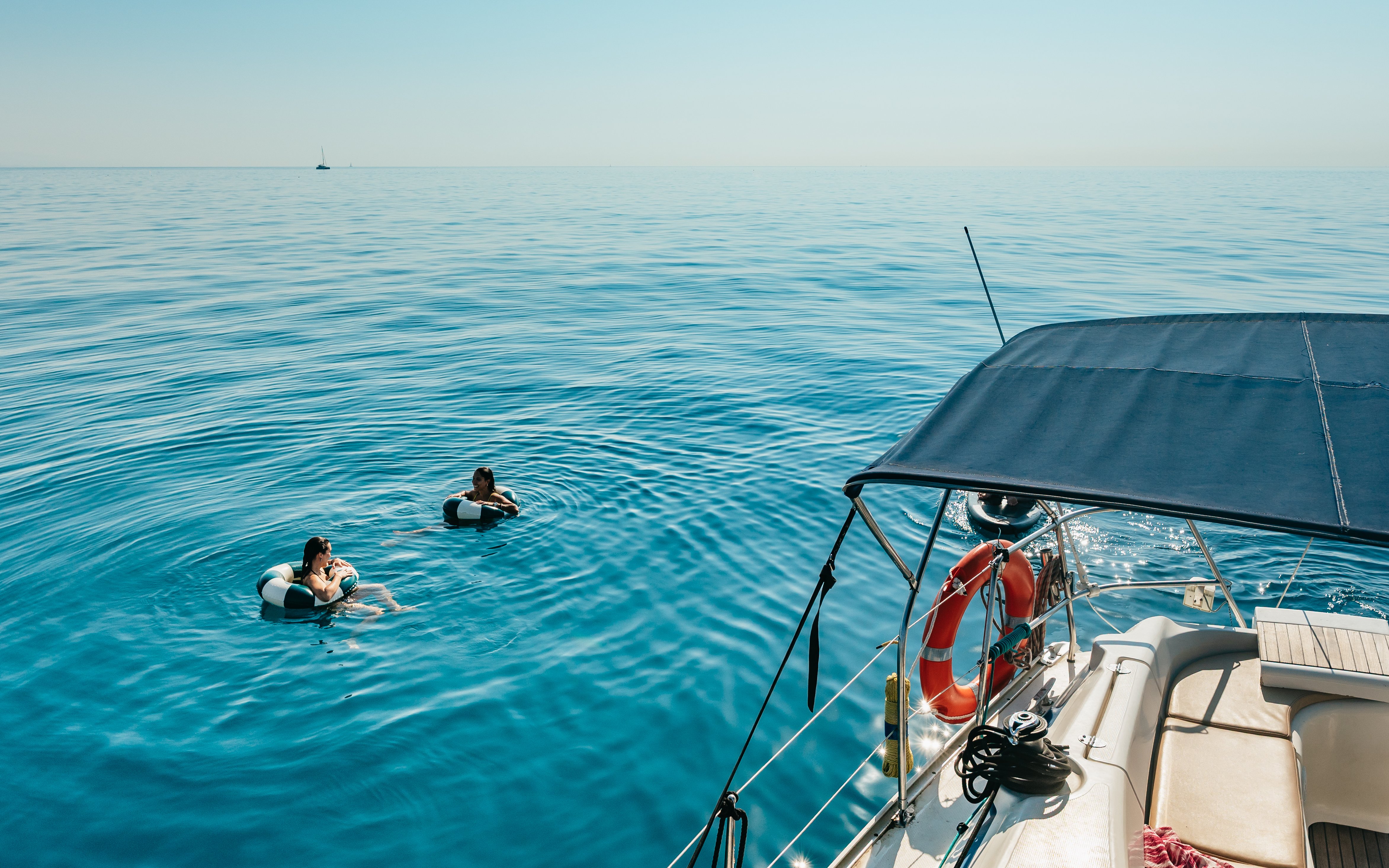 Friends swimming near a sailing yacht on a Barcelona sightseeing cruise.