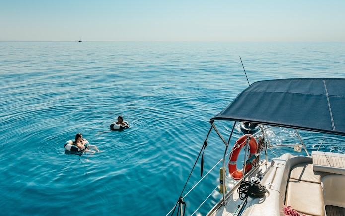 Friends swimming near a sailing yacht on a Barcelona sightseeing cruise.