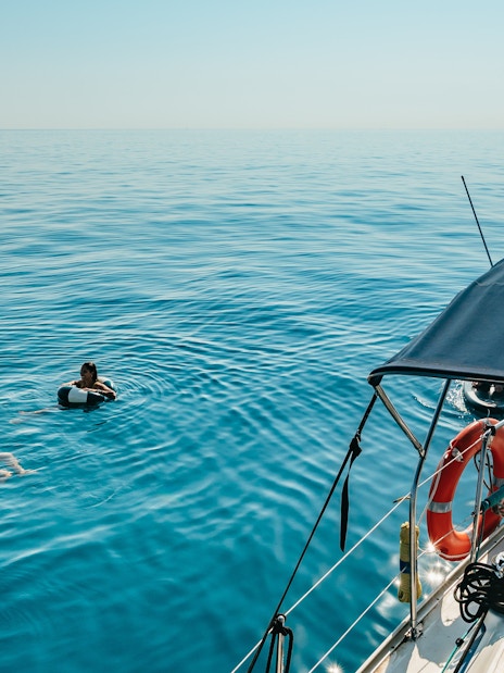 Friends swimming near a sailing yacht on a Barcelona sightseeing cruise.