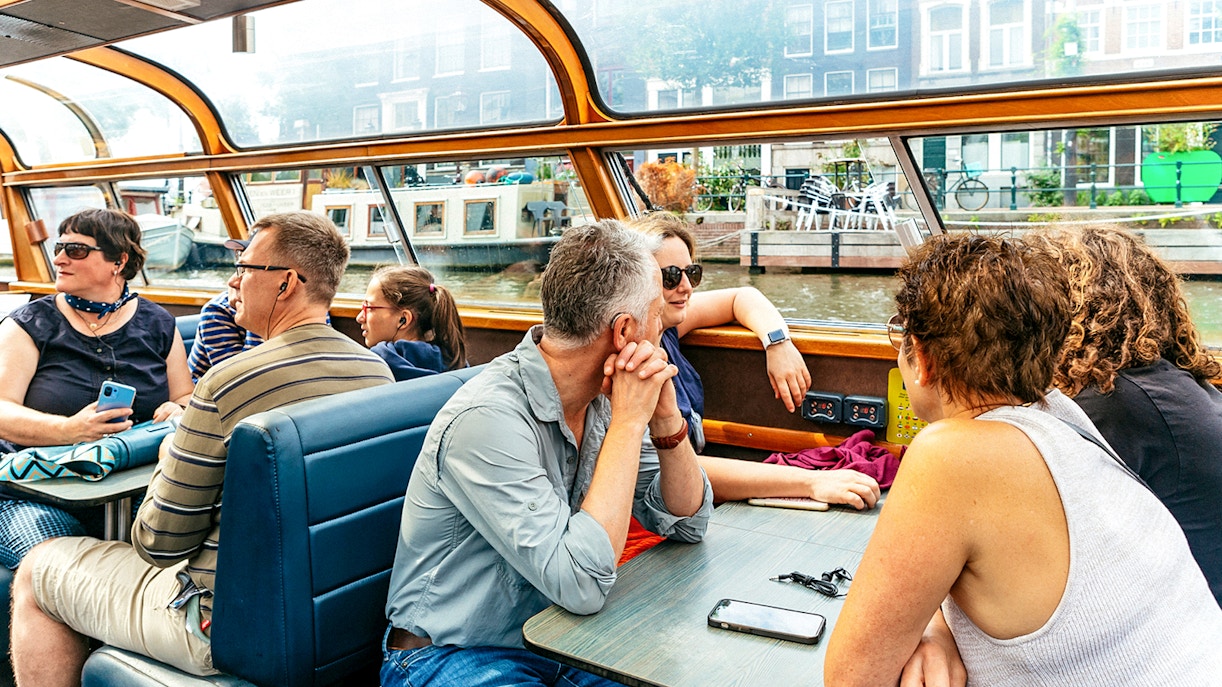 Tourists enjoying a canal cruise in Amsterdam, viewing city architecture.