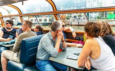 Tourists enjoying a canal cruise in Amsterdam, viewing city architecture.