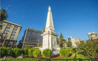 Obelisk on Avenida de Mayo surrounded by buildings and greenery, Buenos Aires.