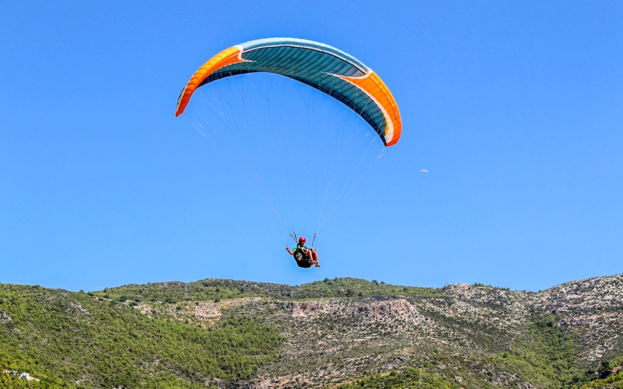 Paraglider soaring over green hills in Alanya, Turkey.