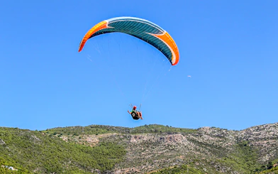 Paraglider soaring over green hills in Alanya, Turkey.