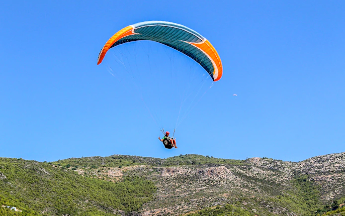 Paraglider soaring over green hills in Alanya, Turkey.