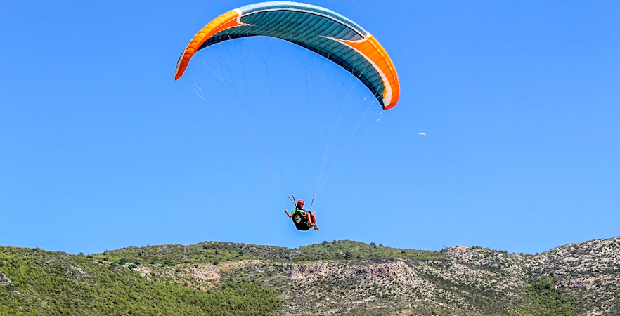 Paraglider soaring over green hills in Alanya, Turkey.