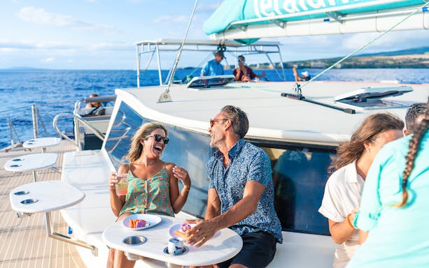Couple enjoying drinks and snacks on a luxury sailboat during a snorkel tour in Maui, Hawaii.