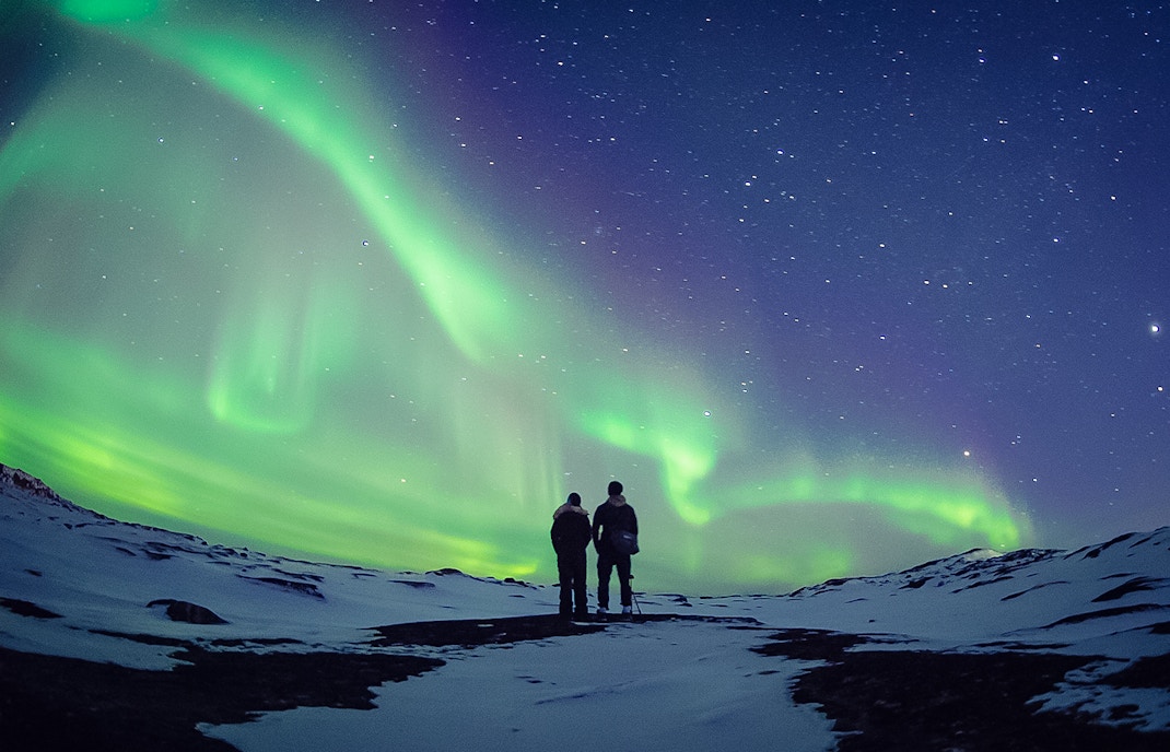 Couple watching Northern Lights in snowy landscape, Aurora Borealis.