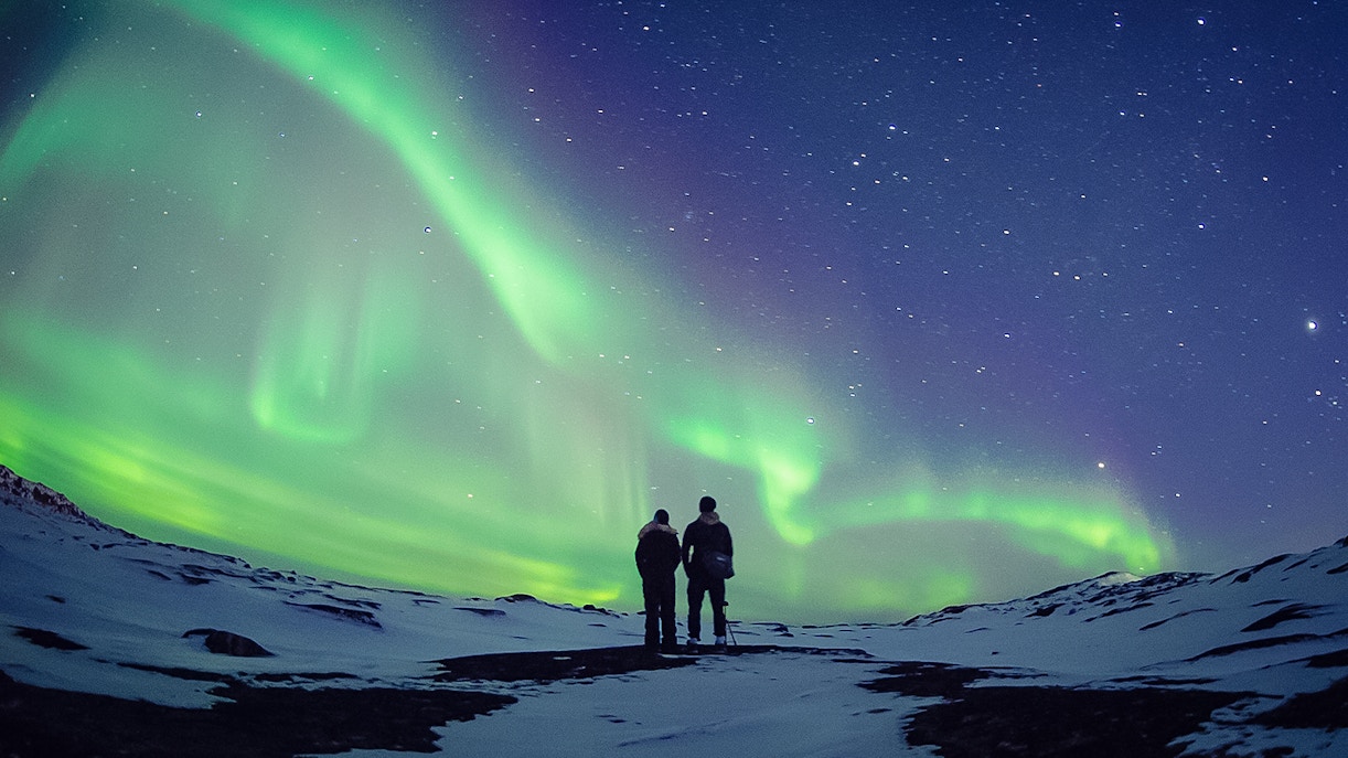 Couple viewing Northern Lights in Norway's winter landscape.