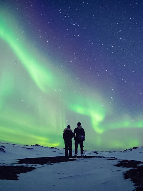 Couple watching Northern Lights in snowy landscape, Aurora Borealis.