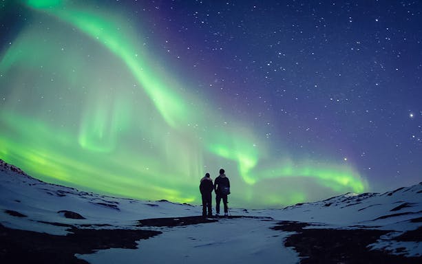 Couple watching Northern Lights in snowy landscape, Aurora Borealis.