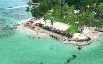 Isla Mamey beach with colorful huts and visitors swimming, part of Panama City tour.