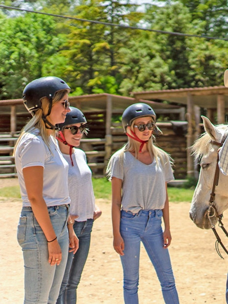 Group learning horse riding with guide and saddled horse in outdoor setting.