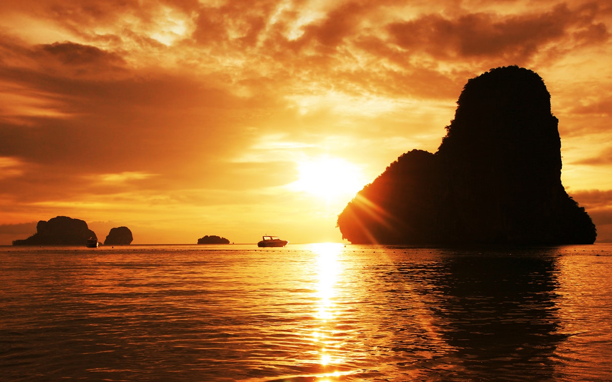 Sunset over limestone cliffs and boat in Krabi, Thailand.