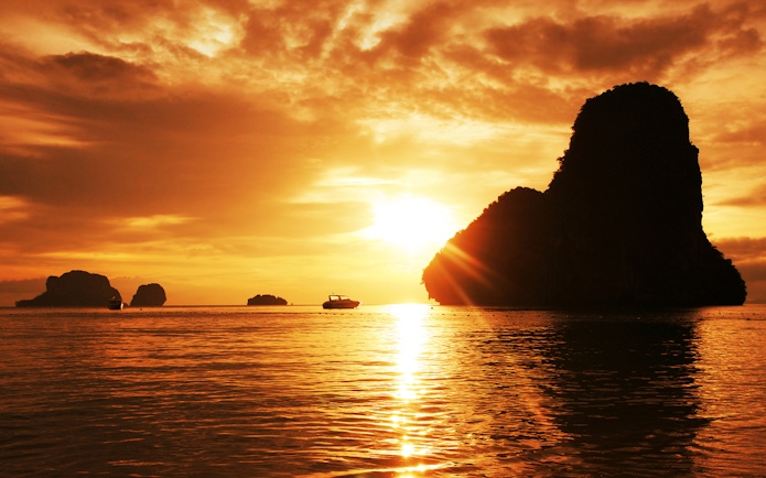 Sunset over limestone cliffs and boat in Krabi, Thailand.
