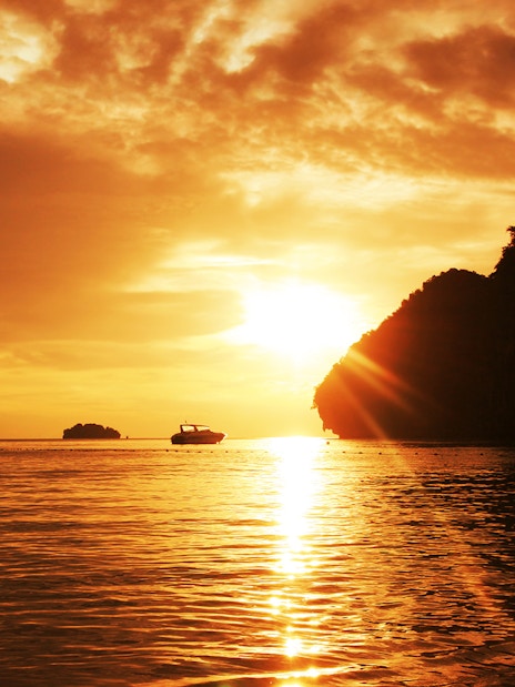 Sunset over limestone cliffs and boat in Krabi, Thailand.