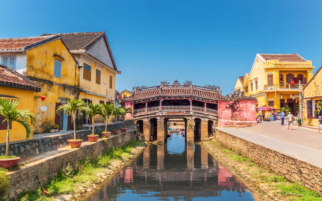 Japanese Covered Bridge over canal in Hoi An, Vietnam, with yellow buildings nearby.